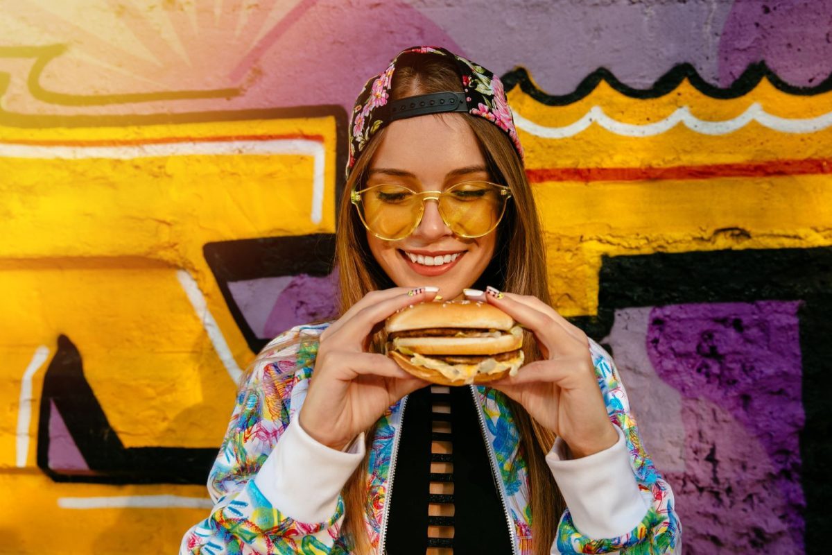 Woman holding burger in from of colorful street art